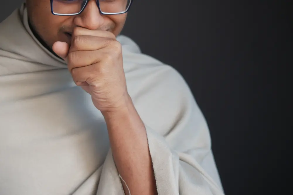 mature man in blanket coughing while sited on bed