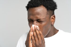 black man sneezing into napkin suffering from seasonal allergy rhinitis has symptoms of cold