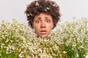 puzzled nervous curly haired young woman surrounded by camomile has allergic reaction on wildflowers